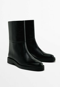 Black leather ankle boots with a smooth finish, rounded toe, minimalistic design, and flat rubber sole. Clean lines and seamless construction.