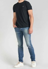 T-shirt nera a maniche corte con scollo rotondo, abbinata a jeans slim fit blu e sneakers bianche, caratterizzata da dettagli minimi e una texture liscia.