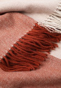 Couverture en laine présentant un motif chevrons en rouge doux et beige, avec des bords frangés et une texture douce.