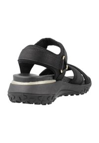 Sandalia negra con un upper de tela texturizada, correas ajustables y una suela acolchada con un dibujo antideslizante para mayor estabilidad.