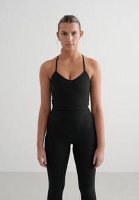 Zwarte geribde sportbeha met dunne bandjes, gecombineerd met hoge zwarte leggings. De gladde textuur en de aansluitende pasvorm creëren een samenhangende look.