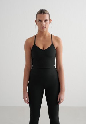 Soutien-gorge de sport noir à côtes avec des fines bretelles, associé à un legging noir taille haute. La texture lisse et la coupe ajustée créent une apparence cohérente.