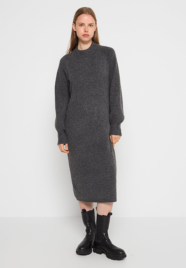 Graues gestricktes Midi-Kleid mit hohem Kragen und langen, gepufften Ärmeln, kombiniert mit schwarzen Stiefeln bis zum Knie. Einfaches, strukturiertes Design.