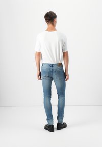 Light blue skinny jeans with a faded finish, paired with a plain white t-shirt. The jeans feature two back pockets and a logo patch.