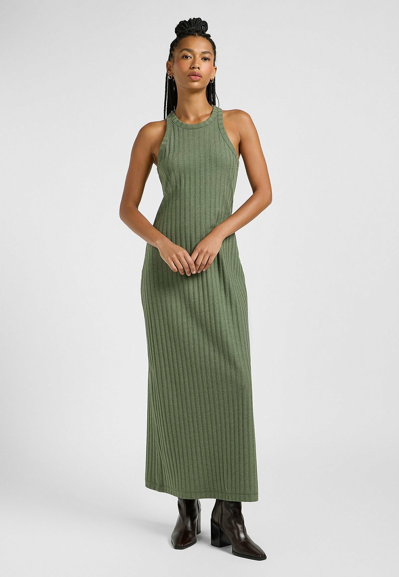 Abito maxi verde a righe, senza maniche e con collo alto, abbinato a stivali ankle boots neri con tacco a blocco.