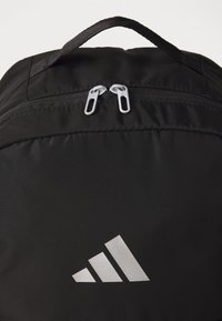 Zaino nero con hardware della zip argentata, superficie in tessuto testurizzato e un logo argento ben visibile sul davanti.