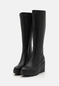 Botas de cuero negras hasta la rodilla con un diseño elegante, tacón de cuña y suela texturizada, que cuentan con un cierre lateral para facilitar su colocación.