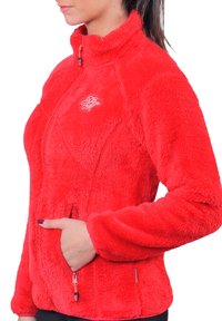 Veste en polaire rouge avec fermeture éclair à l'avant, col haut, poches latérales et détails de fermeture éclair contrastants ; possède une surface texturée et douce.