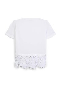 Top bianco a maniche corte con taglio dritto e bordo in pizzo floreale lungo l'orlo inferiore, su uno sfondo bianco semplice.