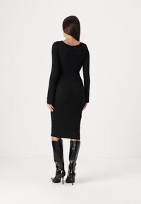 Černé žebrované midi šaty s dlouhými rukávy a otevřenými zády, doplněné černými koženými vysokými podpatky. Hladká textura a přiléhavý střih.