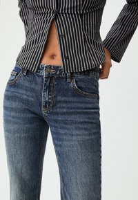 Blue denim jeans with a mid-rise waist, featuring contrast stitching, five-pocket design, and slight fading on the thighs.