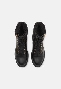 Bottes montantes en cuir noir avec un col en fausse fourrure texturée noire, détails en zip doré et lacets noirs sur une semelle noire lisse.