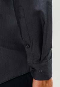 Black dress shirt sleeve with a smooth texture, featuring a buttoned cuff and subtle stitching. Metal buttons are visible, ensuring secure closure.