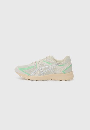 Beige athletic shoe with mesh upper, green accents, and silver detailing. Lightweight sole with textured grip, featuring a sleek, streamlined design.