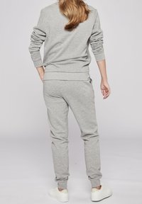 Grå sweatshirt och matchande joggers i mjukt tyg, med ribbade mudd och midjeband. Skorna är vita med en minimalistisk design.