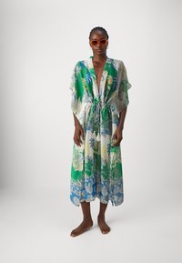 Lång blommig kimono i grön, blå och gul tyg. Har en dragsko i midjan, vida ärmar och en fåll med ett blommönster.