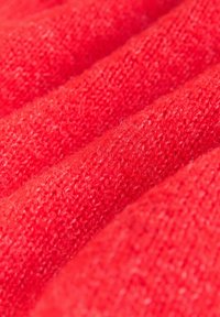 Élénk piros kötött anyag puha textúrával, bordázott vonalakkal és finom szálakkal, barátságos és meleg megjelenést kölcsönözve.