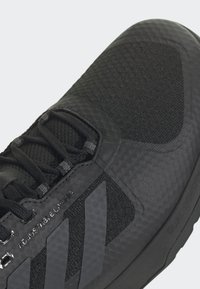 Zapatilla deportiva negra con un material texturizado, sistema de cordones ajustable y un destacado diseño de tres rayas en el lateral.
