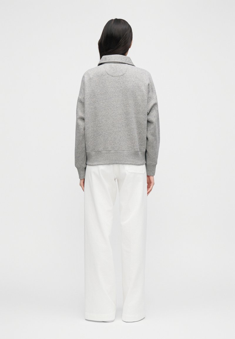 Sweat-shirt gris avec un col large, des poignets et un ourlet côtelés ; associé à un pantalon blanc ample. Tissu doux avec une finition texturée.