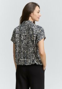 Blusa a maniche corte nera con un motivo astratto beige e bianco, caratterizzata da un colletto e una vestibilità comoda. Tessuto morbido.