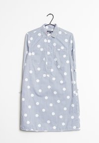 Camisa a rayas en azul y blanco con grandes lunares blancos. Presenta un collar tipo botón y dos bolsillos en el pecho. Tejido de algodón.