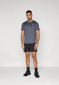 Abbigliamento sportivo da uomo composto da una maglietta grigia a maniche corte e pantaloncini neri. Il materiale sembra leggero; sulla maglietta è presente un logo sul petto.