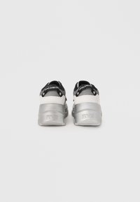 Grå og hvite sneakers med overdel i mesh, tykk sølvsåle og svarte detaljer. Branding synlig på baksiden og stroppen.