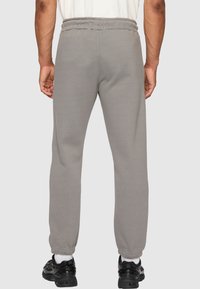 Grå joggebukser med elastisk midje og ankelmansjetter, med en jevn tekstur og en avslappet passform, iført svarte joggesko.