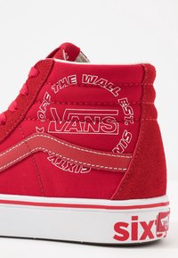 Baskets montantes en toile rouges avec un dessus texturé, des accents rouges unis, une semelle blanche et des logos bien visibles sur le côté et le talon.