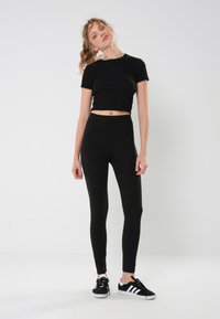 Una maglietta nera crop e leggings neri a vita alta abbinati a sneakers nere. L'outfit è realizzato in tessuto elastico, con una texture liscia.