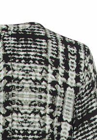 Chemise à motifs présentant des designs abstraits en noir et blanc, avec un tissu texturé et une coupe légèrement ample. Formes et lignes irrégulières notables.