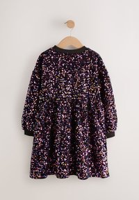 Robe pour enfant en tissu noir recouverte de sequins multicolores, manches longues, encolure ronde, taille froncée, suspendue à un cintre en bois.