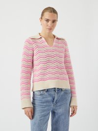 Maglione lavorato a maglia rosa e crema con un motivo ondulato, scollo a V e polsini a costine. Abbinato a jeans di denim blu chiaro.