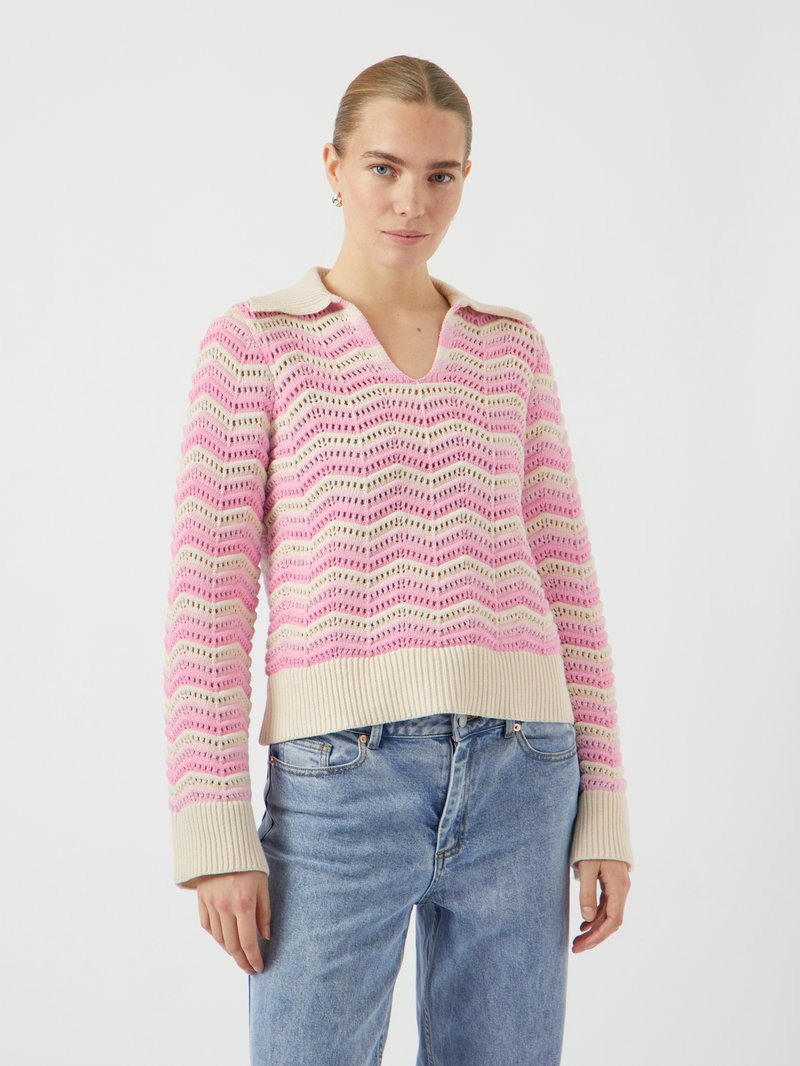 Maglione lavorato a maglia rosa e crema con un motivo ondulato, scollo a V e polsini a costine. Abbinato a jeans di denim blu chiaro.