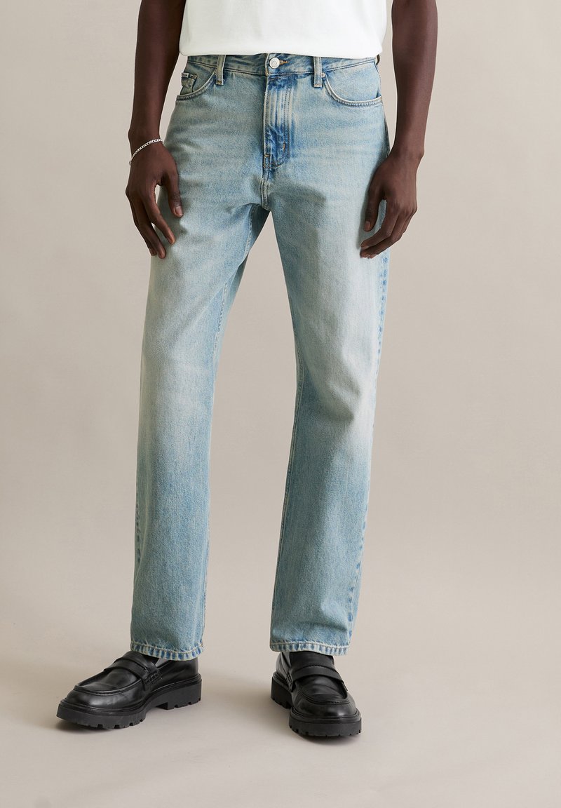 Jeans azzurri a gamba dritta con finitura slavata, design classico a cinque tasche e chiusura con bottone in metallo. Indossati con mocassini neri.