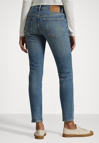 Ljust blå denimjeans med slim fit, utrustade med en brun läderpatch vid midjan och två bakfickor. Slät textur, ankellång.
