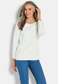 Witte langemouwen top met een ronde hals, gecombineerd met een blauwe spijkerbroek. De stof heeft een gladde textuur. Het ontwerp is casual en aansluitend.