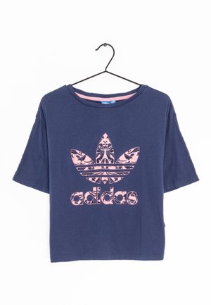 Donkerblauw cropped T-shirt van Adidas met een roze Trefoil-logo met bloemenpatroon en merknaam, hangend aan een zwarte metalen hanger.
