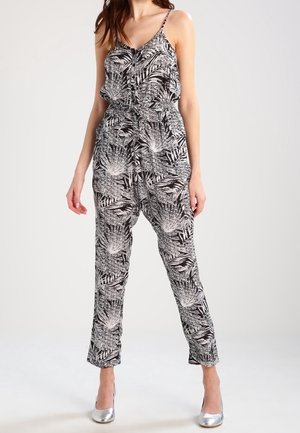 Combinaison noire et blanche avec un motif de feuille de palmier, design sans manches et jambes fuselées. Le tissu semble léger et fluides.