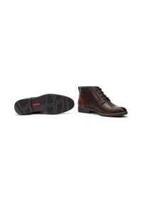 Botas de tobillo de cuero marrón con punta redonda, parte delantera con cordones y forro azul. La suela exterior cuenta con un dibujo de goma negra texturizada.