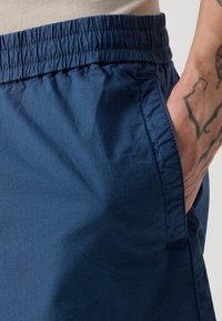 Shorts bleu marine en tissu léger avec une taille élastique. Comprend une poche latérale et une texture subtile pour plus de confort.