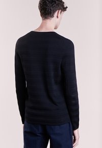 Pull noir à manches longues avec un motif de rayures horizontales texturées, un col rond et une coupe ajustée. Texture lisse avec un léger éclat.