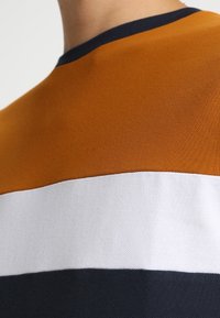 Košile s krátkým rukávem s vodorovnými pruhy v oranžové, bílé a námořnické modři. Texturovaná tkanina s kulatým výstřihem a kontrastním límečkem.