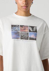 Camiseta branca de algodão com estampa gráfica de seis imagens quadradas com temas da natureza, texto "ETHEREAL METAMORPHOSIS" e design de ajuste relaxado.