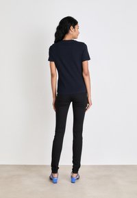 Marineblå kortermet skjorte, tettsittende design. Brukt med svarte smale jeans og blå hælsandaler. Enfarget uten synlige mønstre eller detaljer.