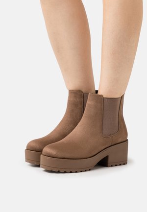 Botas de tobillo de ante marrón con una plataforma gruesa, paneles laterales elásticos y una puntera redondeada. La suela tiene un agarre texturizado para mayor tracción.