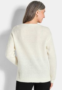 Weißer Strickpullover mit lockerer Passform, der über eine gerippte Textur und lange Ärmel verfügt. Der Rücken hat einen klassischen Rundhalsausschnitt und subtile diagonale Muster.