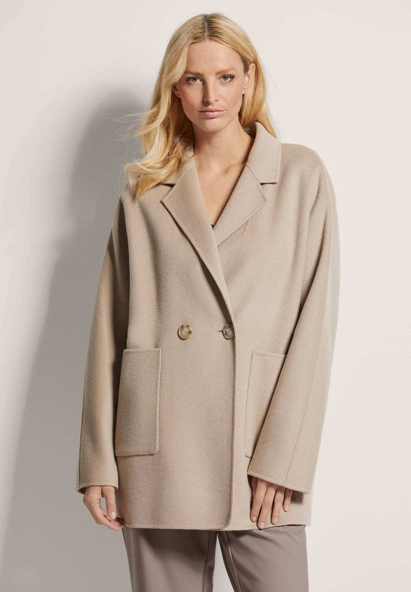 Beige oversized wollen mix jas met een reverskraag, dubbele knoopsluiting en twee voorzakken. Zachte textuur en relaxte pasvorm.