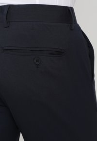 Dunkelblaue Hosen mit glatter Textur, ausgestattet mit einer hinteren Tasche mit Knopfverschluss und einer taillierten Passform an der Taille.