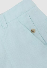 Lyseblå linnedbukser med linning, bæltestrop, sidelomme og beige knapdetalje.
